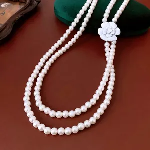 Double-layered glass pearl necklace with white camellia pendant on brown leather background
