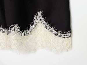 Detail shot of delicate white lace trim on luxurious black satin fabric for elegant top