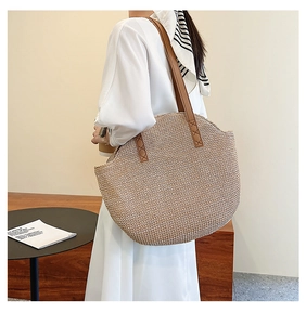 Detail of hand-woven straw tote bag with brown leather handles and reinforced stitching