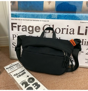 Detail of durable black nylon crossbody bag featuring adjustable strap and orange side label