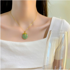 Detail of a gold titanium necklace with a green jade-style pendant on a female model