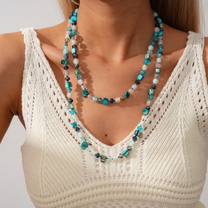Détail d'un collier de perles bohème avec cristaux bleus sur un haut en crochet blanc
