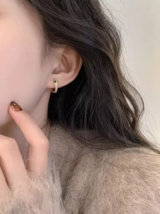 Close-up of snake textured gold hoop earring with white diamonds and green gemstone
