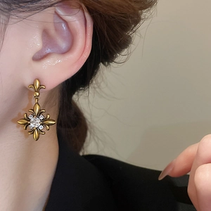 Detail view of vintage gold fleur-de-lis earrings with shimmering zircon and aged finish