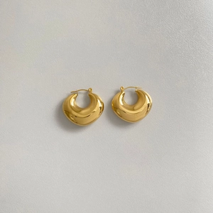 Detailed close-up of golden hollow oval stud earrings on white textured background