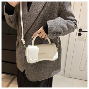 Detail view of a white leather crossbody bag with gold FASHION lettering on gray blazer