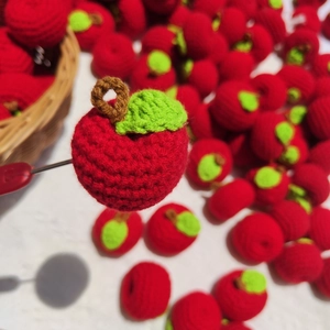 Close-up of a handmade red crochet apple pendant with green leaf and brown stem detail