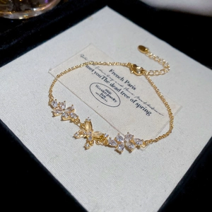 Macro detail of 18k gold plated bracelet with zircon flowers and a butterfly charm