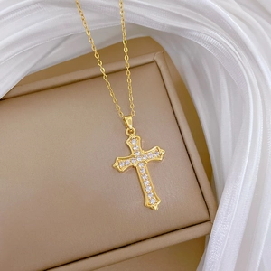 Detailed view of a gold-plated cross necklace with zircon stones on silk fabric
