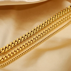Three widths of golden Cuban link anklets displayed on luxurious silk fabric textures
