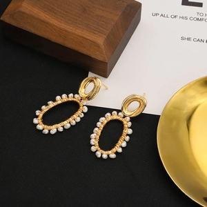Elegant gold earrings with white woven pearls displayed on a sophisticated black background