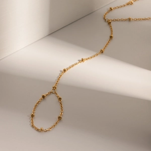 Detail of gold slave bracelet with small metal beads and ring on white background