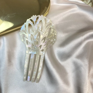 Close-up of white acetate hair comb with shell luster on elegant silk background
