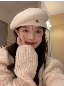 Close-up of white wool beret featuring a classic oval metal M logo decoration