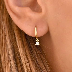 Close-up of 18K gold hoop earrings featuring a sparkling round zircon stone drop