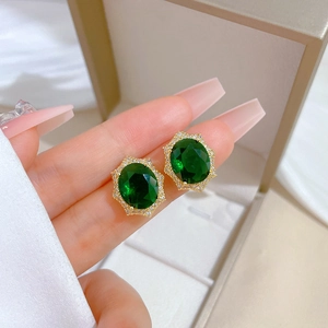 Macro shot of gold-plated stud earring with emerald green gem and white zircon halo