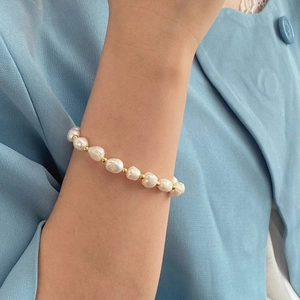 Macro shot of Baroque pearl bracelet with golden beads on a model wearing light blue
