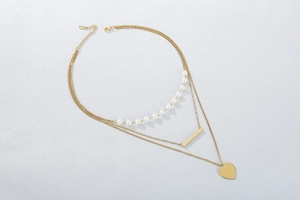 Detail of layered gold necklace with heart pendant, bar charm, and elegant pearls