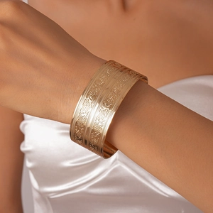 Macro detail of gold open bangle with intricate vintage floral relief and geometric patterns