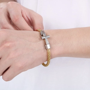 Detail of a twisted cable gold bracelet featuring a silver cross charm and metal beads