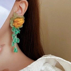 Gros plan d'une fleur en tissu jaune et de boucles d'oreilles à pompons en perles vertes