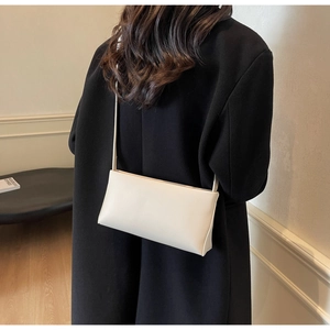 Minimalist cream white rectangular crossbody bag styled with a sleek black coat