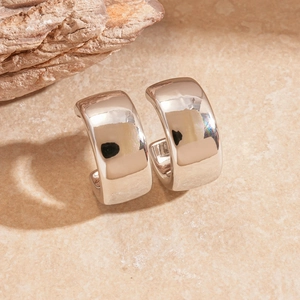 Polished silver C-shaped chunky hoop earrings displayed on a natural stone surface
