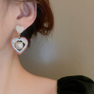 Détail de boucles d'oreilles cœur vintage avec bord rouge, perles bleues et grande perle