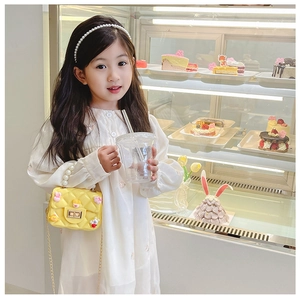 Little girl holding a yellow quilted crossbody bag with pearls and cartoon charms