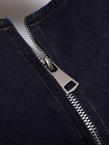 Detailed macro view of metal zipper and yellow stitching on dark blue denim dress