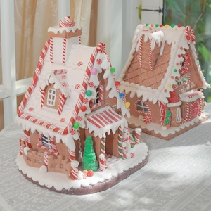 Lighted Christmas gingerbread house ornaments with miniature trees on lace tablecloth