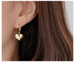 Close-up of a model wearing the gold heart drop earrings with a vintage metallic finish
