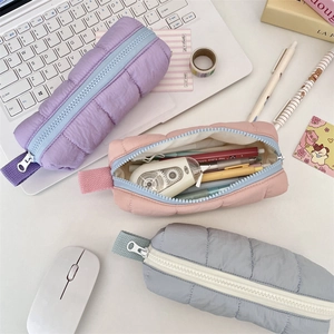 Detailed view of quilted puffer pencil pouches in lilac, peach, and light grey colors