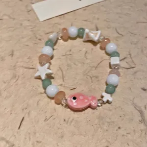 Detail of beaded bracelet featuring a pink ceramic fish charm and colorful beads