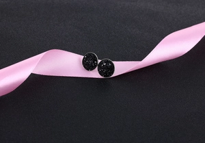 Macro detail of black crystal stud earrings on a pink silk ribbon with textured background