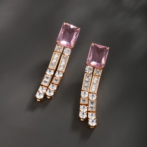 Detailed macro of long gold drop earrings featuring pink rectangular gems and clear zircons