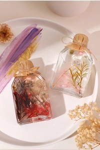 Artistic close-up of reed diffuser bottles with botanicals in a white decorative tray