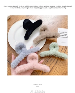 Hand holding a plush large hair claw clip in various colors on a wooden table