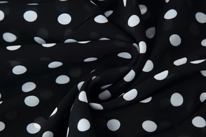 Detailed close-up of lightweight black chiffon fabric with classic white polka dot pattern