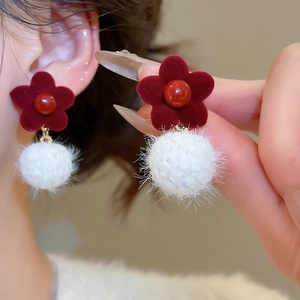 Close-up of red velvet flower earrings with white faux fur pom poms and pearl accents