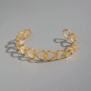 Macro detail of 18K gold plated hollow heart charm on minimalist open bangle bracelet