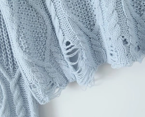 Close-up of light blue cable knit sweater with distressed hole details and fringe texture