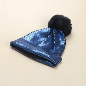 Dettaglio di un berretto in maglia blu metallizzato con un soffice pompon nero