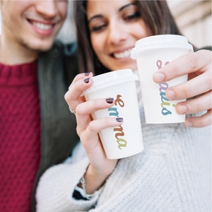 Close-up of custom white paper cups with colorful cursive names Emma and Sakis