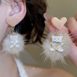 Detail showing plush teddy bear and pompom earring with heart stud on model ear
