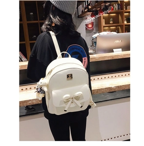 Back view of a white leather backpack featuring bow detail and a small bear plush charm