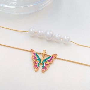 Collana chic a strati dorata con ciondolo a farfalla e perle su tessuto bianco strutturato