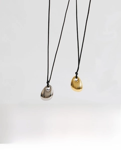Close-up of gold and silver bean pendants with mirror finish on black cord necklaces