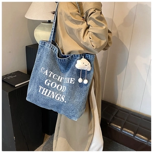 Detail view of denim tote bag featuring slogan and cloud plush keychain accessory