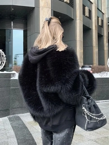 Back view of black faux fur hooded coat with wide sleeves in an urban winter setting